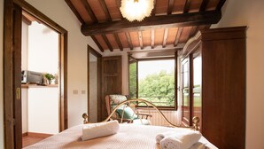 A bedroom with a bed, a chair, a window, and a wooden ceiling.