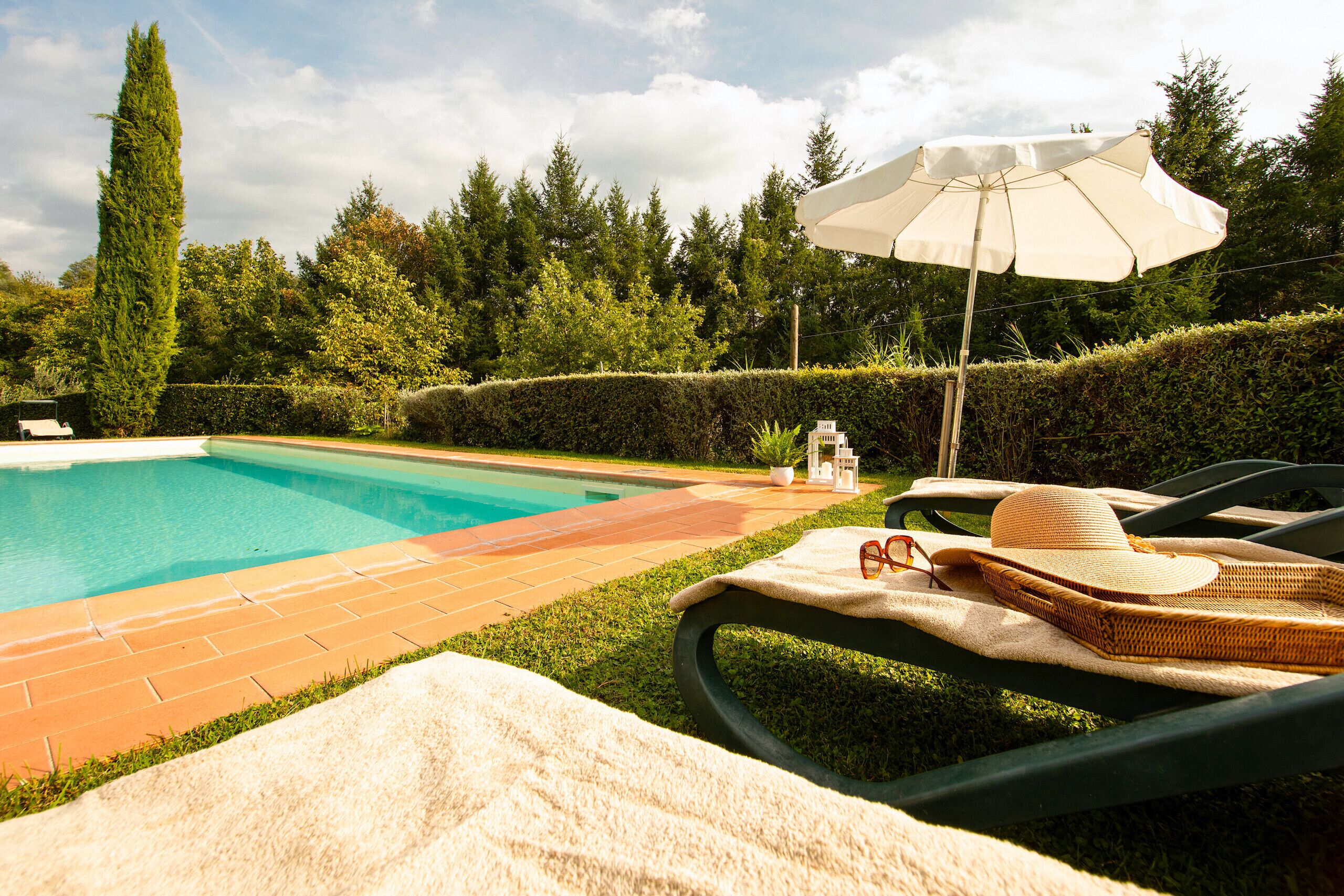 Piscina con sillas de descanso y una sombrilla, rodeada de follaje.