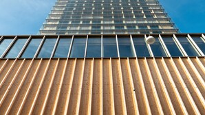 Un edificio alto de diseño moderno, con fachada de vidrio y estructura de madera ranurada en la base.