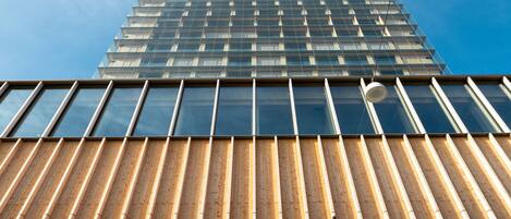 Un edificio alto de diseño moderno, con fachada de vidrio y estructura de madera ranurada en la base.