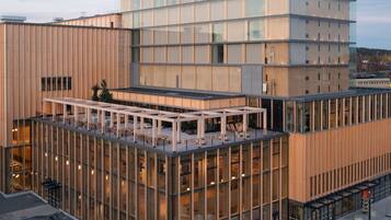 A modern building with a glass facade, a rooftop terrace, and a multi-story structure.
