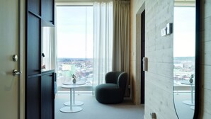 Una habitación de hotel moderna con un ventanal grande, una mesa redonda, una silla cómoda y un espejo en la pared.