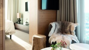 Una habitación de hotel moderna con paredes de madera, un televisor de pantalla plana sobre una ventana, una butaca mullida y dos mesitas con adornos.