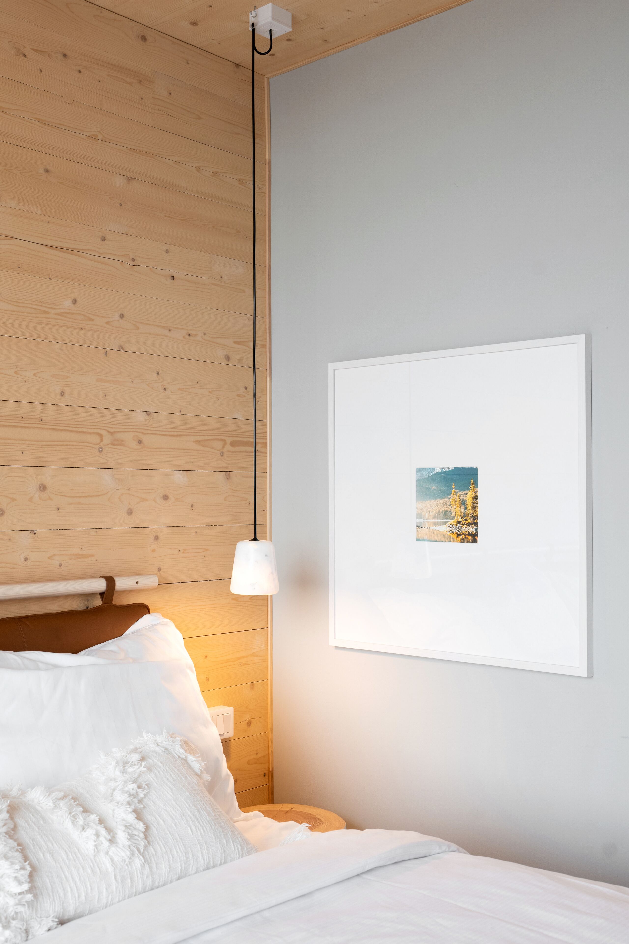 A bedroom with a wooden headboard, a white bedspread, and a framed picture on the wall.