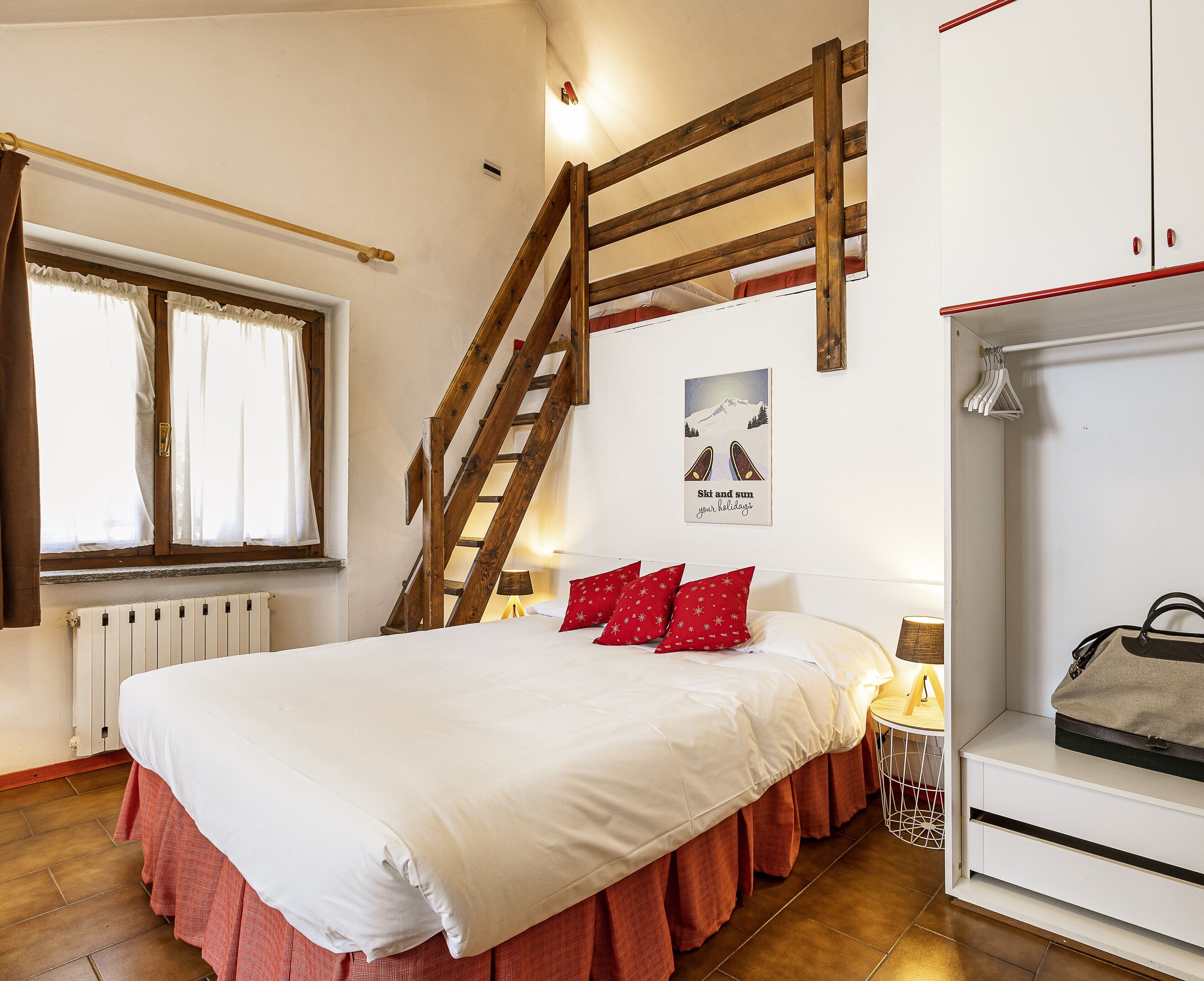 A bedroom with a wooden staircase, a bed with red pillows, a radiator, and a wardrobe.