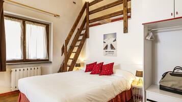 A bedroom with a wooden staircase, a bed with red pillows, a radiator, and a wardrobe.