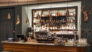 Una zona de bar con mostrador de madera, varios taburetes, una variedad de botellas y vasos, y una cabeza de ciervo montada en la pared.