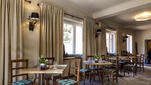 Un comedor con mesas y sillas de madera, cortinas beige e iluminación montada en la pared.