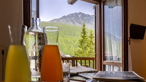 Una mesa con bebidas, vasos y periódicos junto a una ventana con vistas a la montaña.