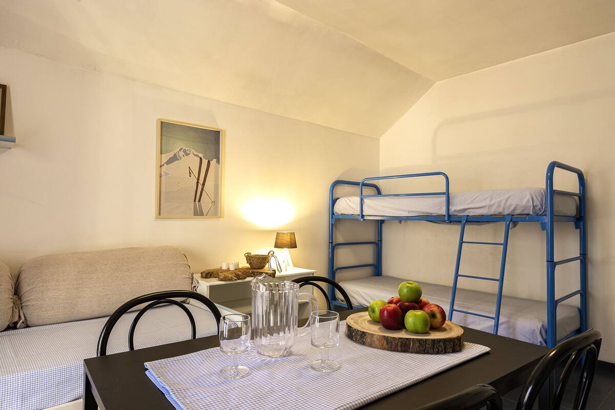 Habitación con literas, una mesa para dos personas, una lámpara y un cuadro en la pared.