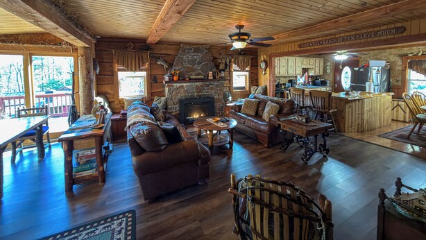A cozy cabin interior with a stone fireplace, wooden furniture, and a kitchen area.