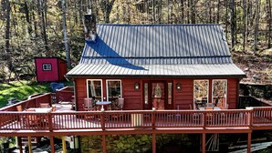 A cabin with a deck, a small red shed, and a car parked nearby.