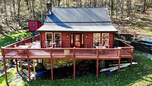 A wooden cabin with a metal roof, a deck, and a small red shed in a forested area.