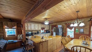A cabin-style kitchen with wooden cabinets, a central island, and a dining area with wooden chairs.