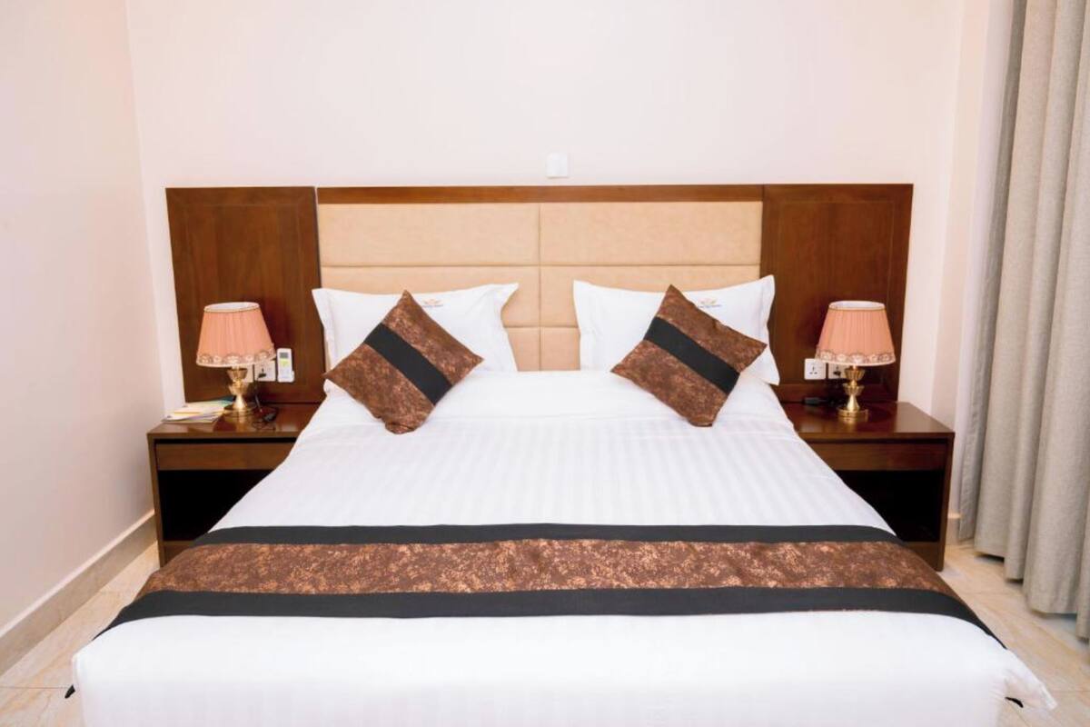 Quarto de hotel com uma cama grande, duas mesas de cabeceira com luminárias e uma cabeceira de madeira.