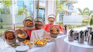 Una mesa de buffet con cestas de pan, bollería y fruta, y varias cafeteras de acero inoxidable.