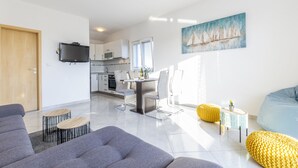 A modern living room with a grey sofa, a dining area with a table and chairs, a kitchen in the background, and a painting of sailboats on the wall. - Villa Spark **** with pool in Rogoznica / Zečevo (Rogoznoca)