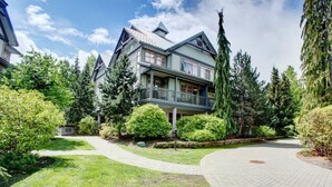 Ein großes, zweistöckiges Haus mit Balkon, umgeben von üppiger Vegetation und Bäumen.