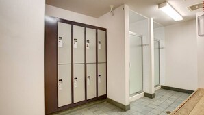 Ein Hotelbad mit einer Reihe von Schließfächern, einem Duschbereich und einer hölzernen Sitzbank.