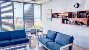 Un salon moderne avec vue sur la plage, un coin repas et des étagères à livres.