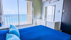 Une chambre à coucher avec un grand lit, une commode, un miroir et une vue sur l’océan par une porte coulissante.