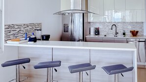 Une cuisine moderne dotée d’un îlot central, d’appareils électroménagers en acier inoxydable et d’un coin bar avec des tabourets.