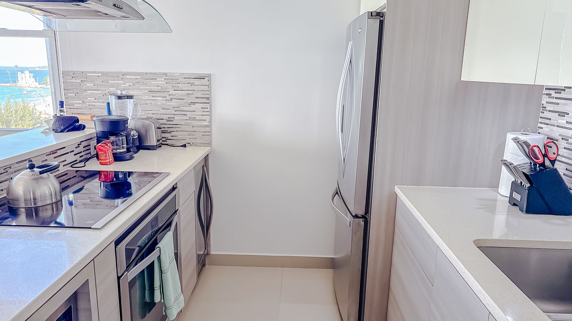 A modern kitchen with a stainless steel refrigerator, a kettle, a toaster, and a coffee maker on the counter.