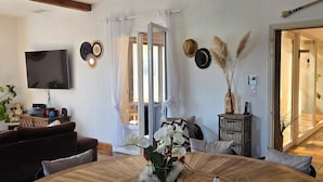 Een woonkamer met een televisie, bank en een eettafel met een bloemenvaas.