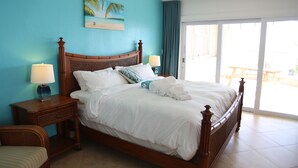 Une chambre à coucher avec un lit, des tables de chevet, une lampe, une chaise et une vue sur l’extérieur.