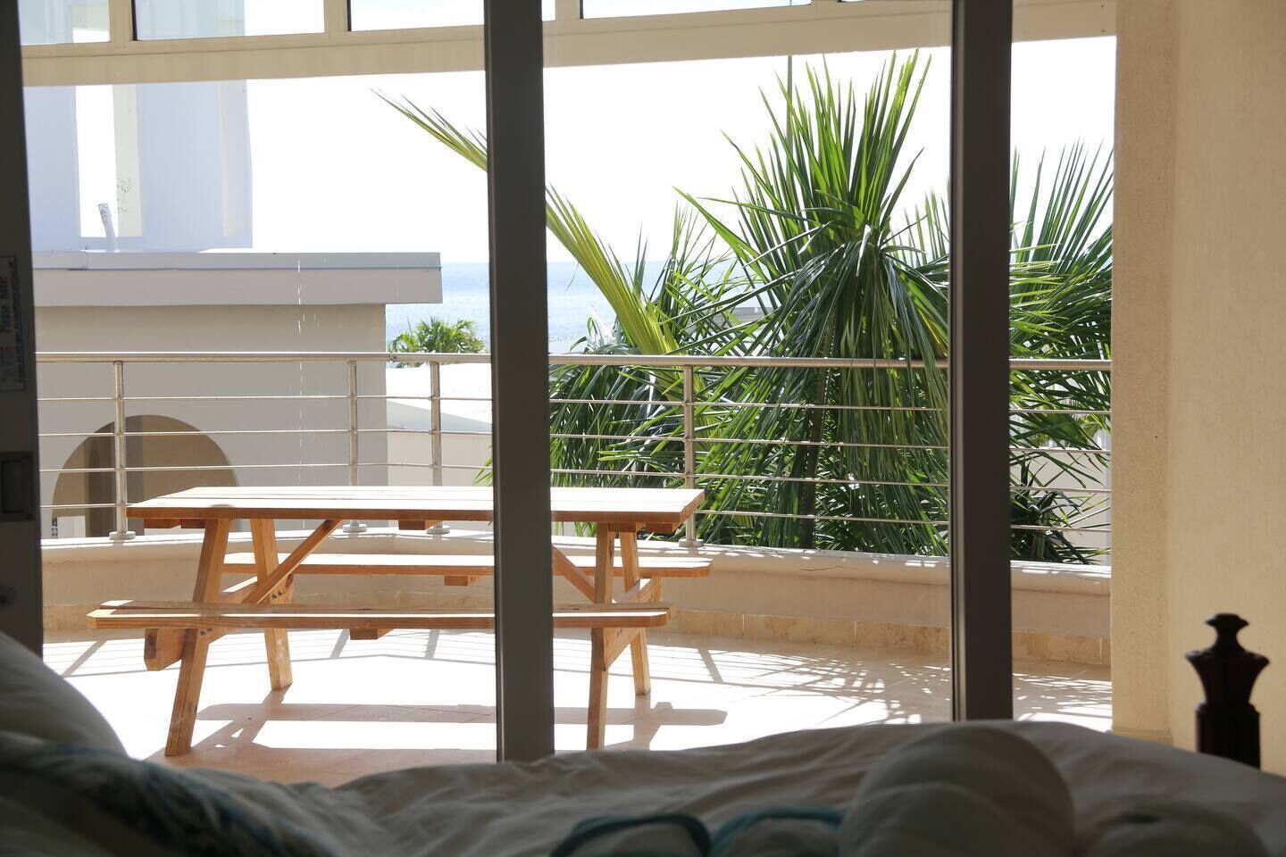 Un balcón con mesa y sillas de madera, con vistas a un jardín con palmeras.