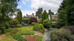 Ein Garten mit Kiesweg, verschiedenen Sträuchern und hohen Bäumen.