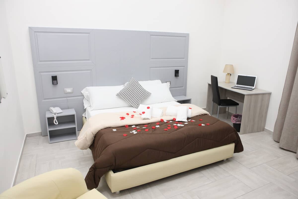 A modern hotel room with a bed, bedside table, lamp, and a desk with a laptop.