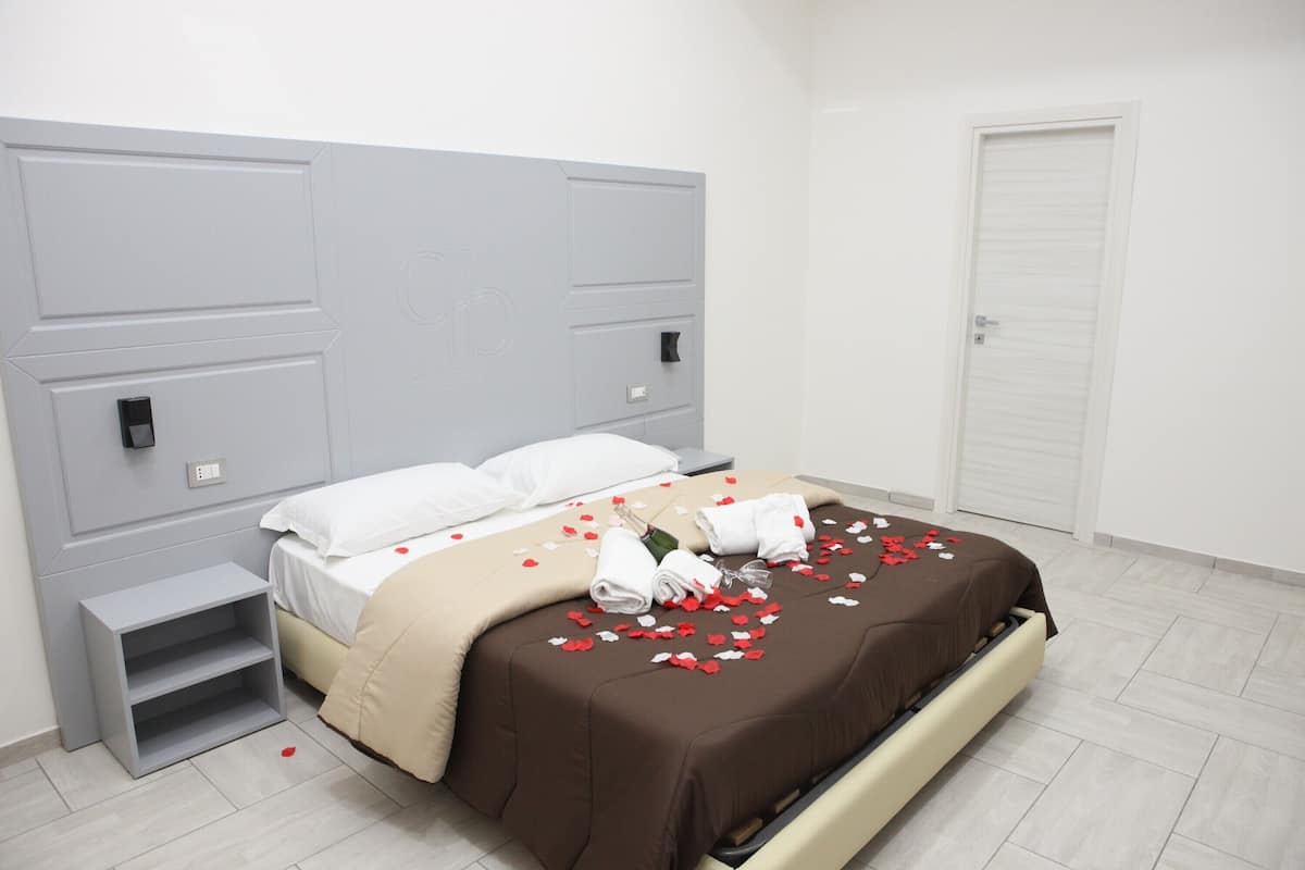 A neatly made bed with white and brown bedding, a bedside table, and a wardrobe in a modern hotel room.