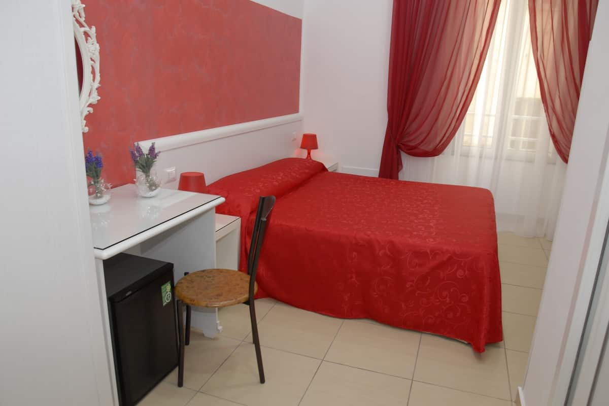 A small, neatly arranged bedroom with a single bed, a desk, a chair, and a small refrigerator.