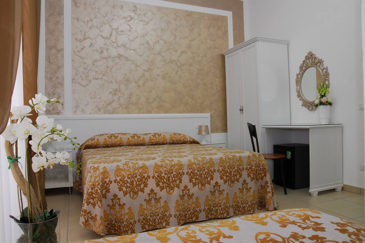 A bedroom with a bed, a desk, a chair, a wardrobe, and a mirror.