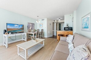 Ein Wohnzimmer mit Fernseher, Essbereich, Küche und einer Couch.