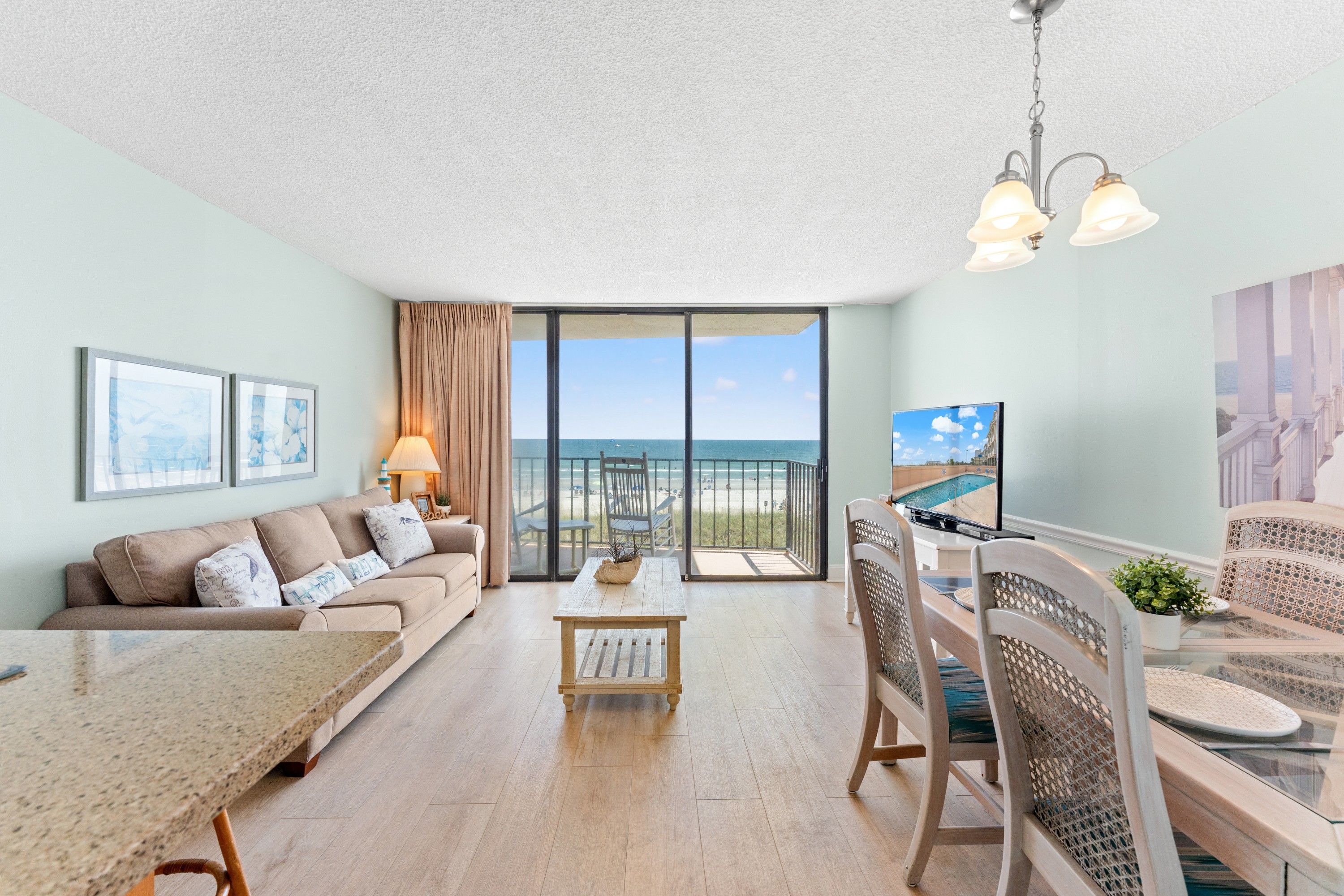 Un vaste salon avec un balcon donnant sur la plage, un coin repas avec vue et un téléviseur fixé au mur.