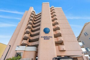 Un edificio de gran altura con un diseño arquitectónico distintivo, que presenta una columna central con el nombre "CAROLINA REEF" y un logotipo con forma de concha.