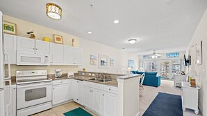 A modern kitchen with white cabinetry, a built-in oven, and a microwave. There is a blue rug on the floor and a blue couch in the living area.