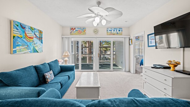 A living room with a blue sofa, a white coffee table, and a ceiling fan. There is a sliding glass door leading to an outdoor area.