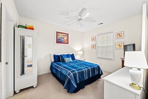 A bedroom with a bed, a nightstand, a desk, a ceiling fan, and a wardrobe.