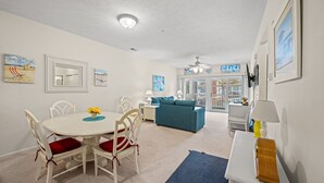 A dining area with a white table and chairs, a blue sofa, and a small lamp on a white console.