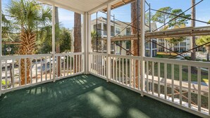 A covered outdoor area with a green floor, white railings, and views of surrounding buildings and trees.