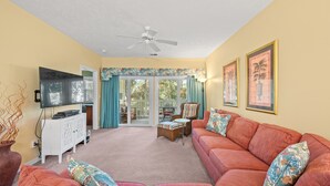 A living room with a red sofa, a television, and a ceiling fan. - Ocean Keyes 4424 - Walk to Beach - 2 Bedroom Condo (North Myrtle Beach)