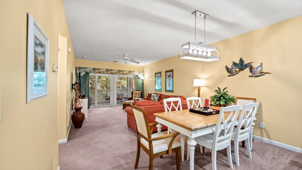 A dining area with a wooden table and white chairs, a ceiling fan, and a hanging light fixture. - Ocean Keyes 4424 - Walk to Beach - 2 Bedroom Condo (North Myrtle Beach)