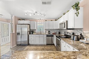 Una cocina moderna con electrodomésticos de acero inoxidable, armarios blancos y encimera de granito.
