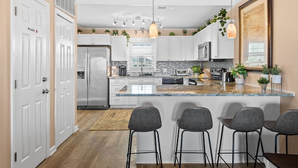 A modern kitchen with white cabinets, stainless steel appliances, a granite countertop, and bar stools. - Barbee's Flamingo-4 Bedroom/2 Bath Channel House in Cherry Grove (North Myrtle Beach)