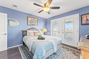 A bedroom with a bed, a ceiling fan, a window with blinds, and a door.