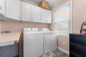 A laundry room with a washer and dryer, cabinets, a window with blinds, and a fire extinguisher. - Barbee's Flamingo-4 Bedroom/2 Bath Channel House in Cherry Grove (North Myrtle Beach)