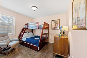 A bunk bed with a desk and chair, a window with blinds, and a painting on the wall.